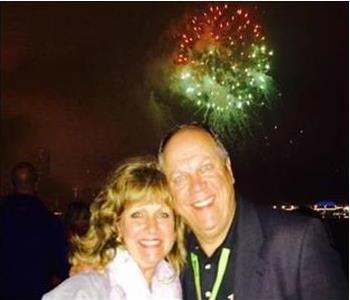 Man and women stand hugging with fireworks going off behind them 